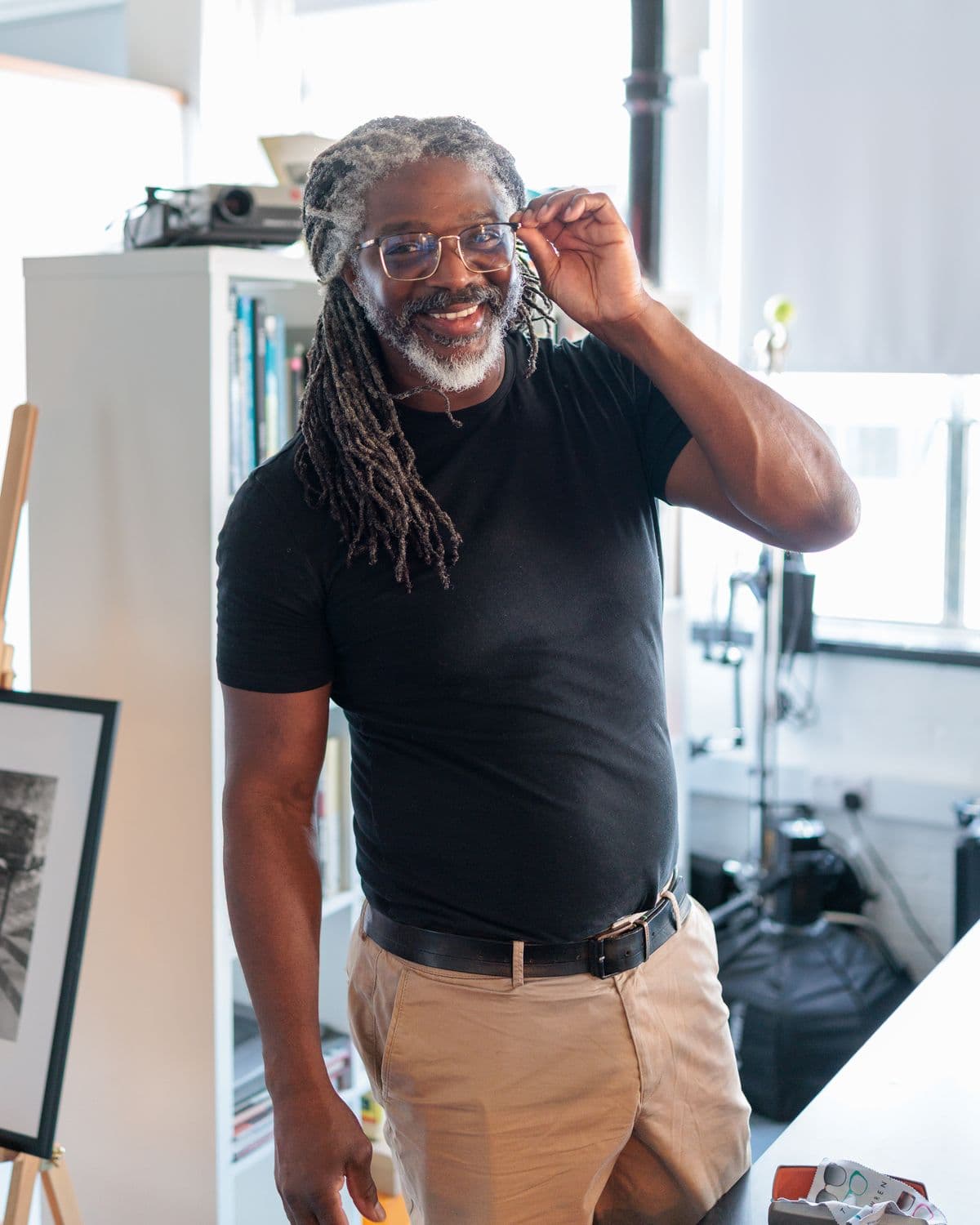Kevan smiling at the camera, adjusting his glasses, in the studio with a light on a stand behind him