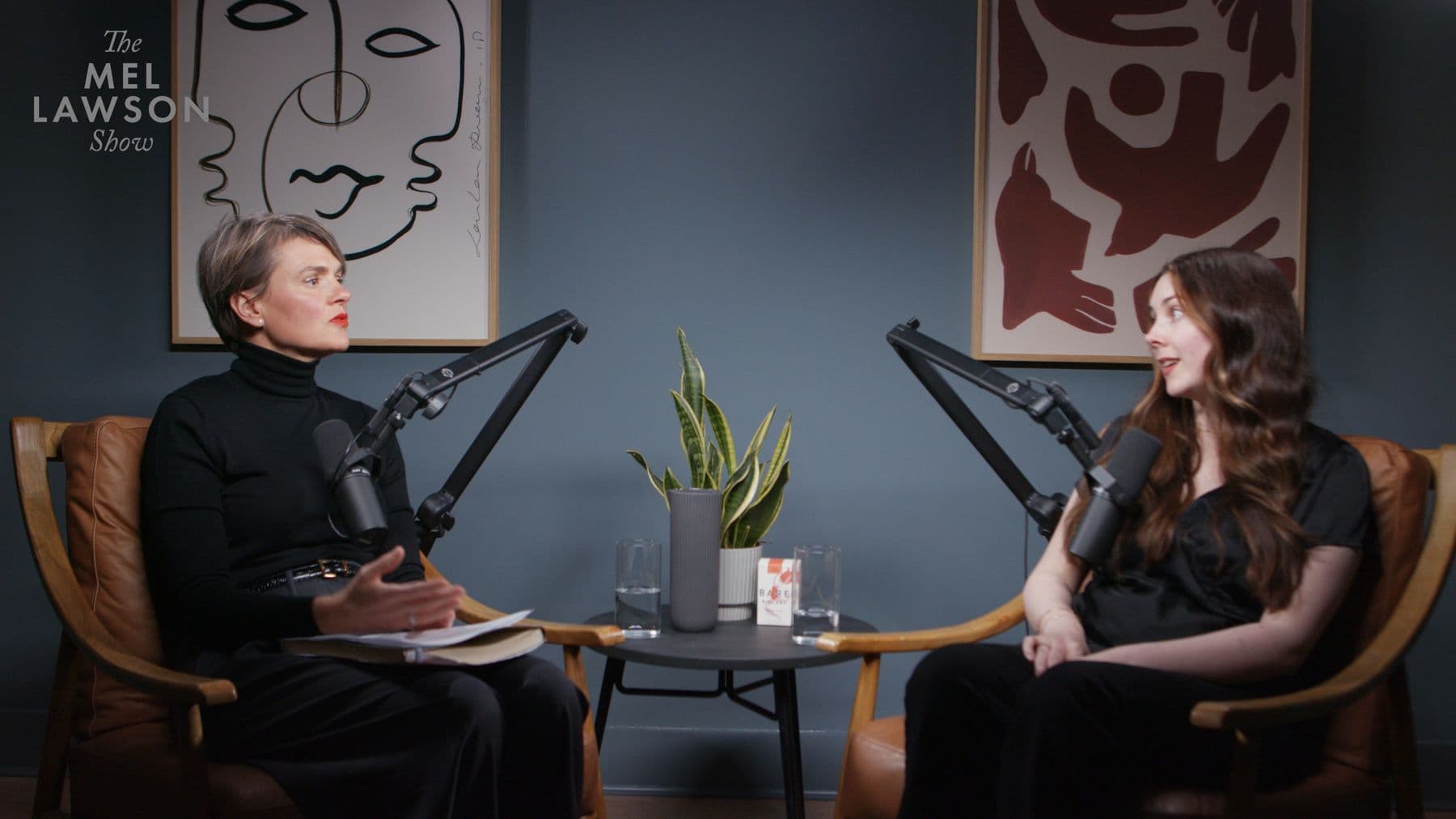 The wide camera angle from episode four: Mel Lawson and Liv Evans in two chairs either side of a low table, the show's logo in the top corner
