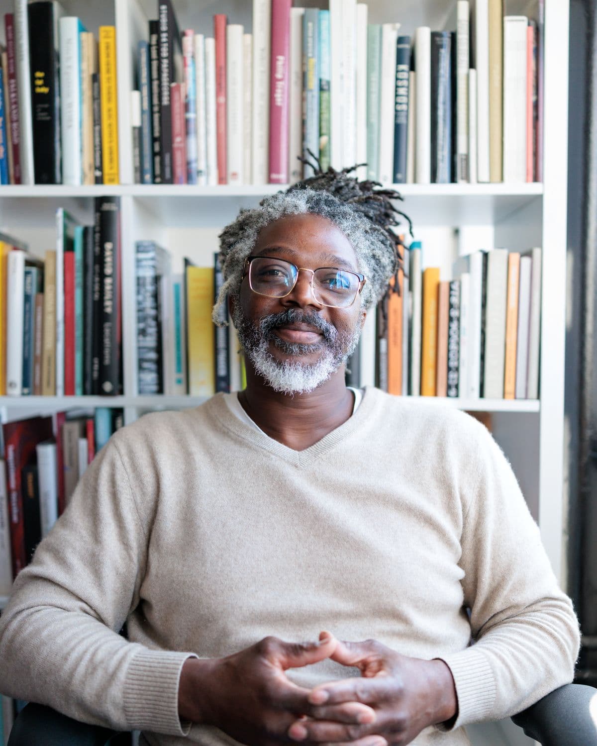 Kevan seated at a table in front of a wall of books, hands clasped, listening