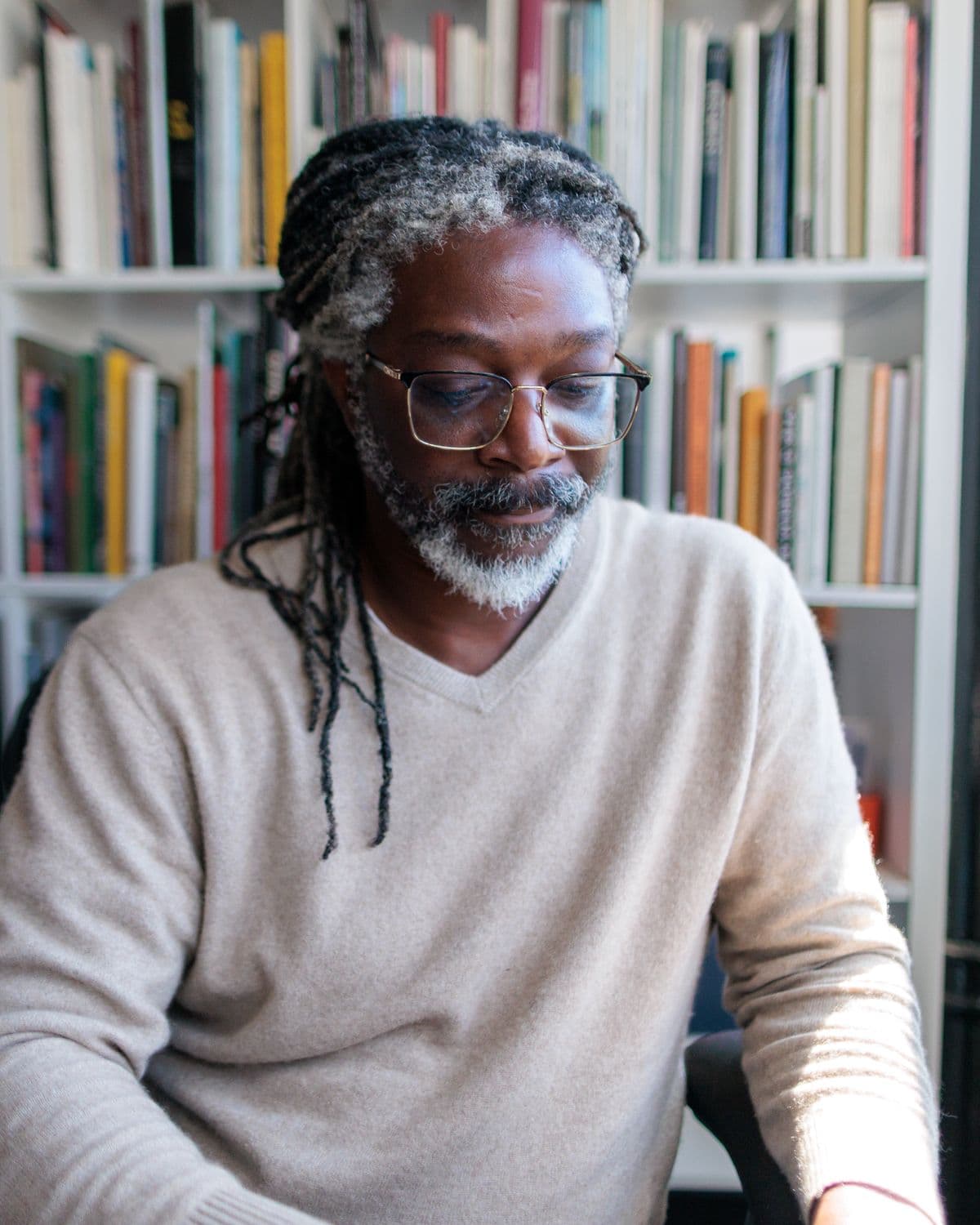 Kevan at his desk in front of a wall of books, glasses on, looking down at his work