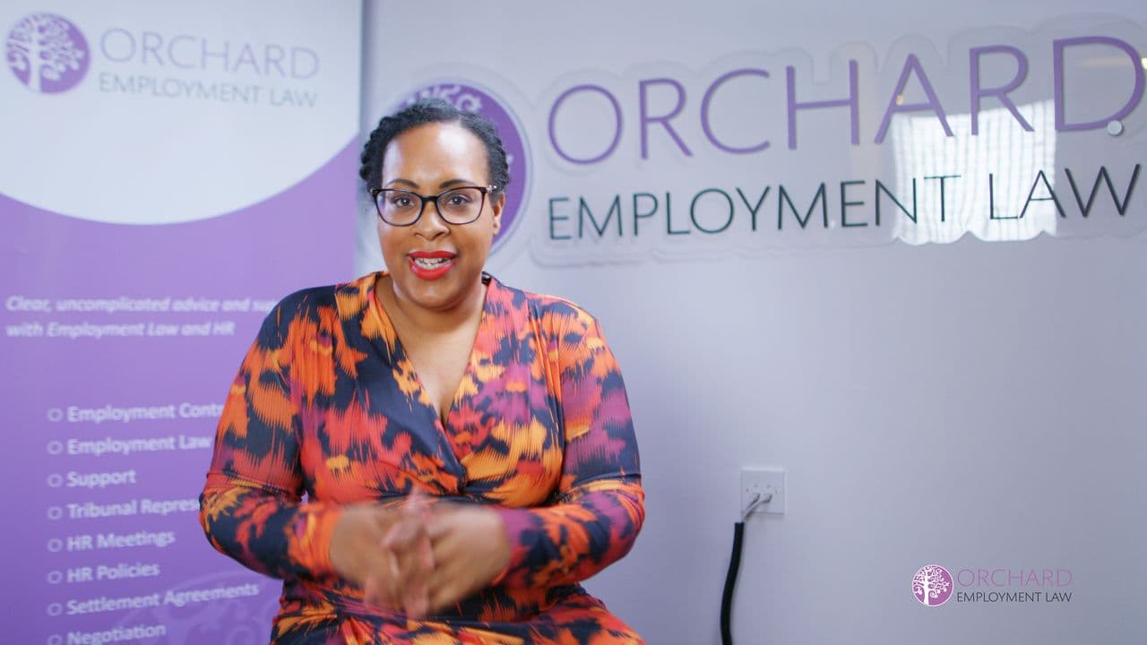 Jemma seated in front of the purple Orchard Employment Law banner, smiling as she speaks