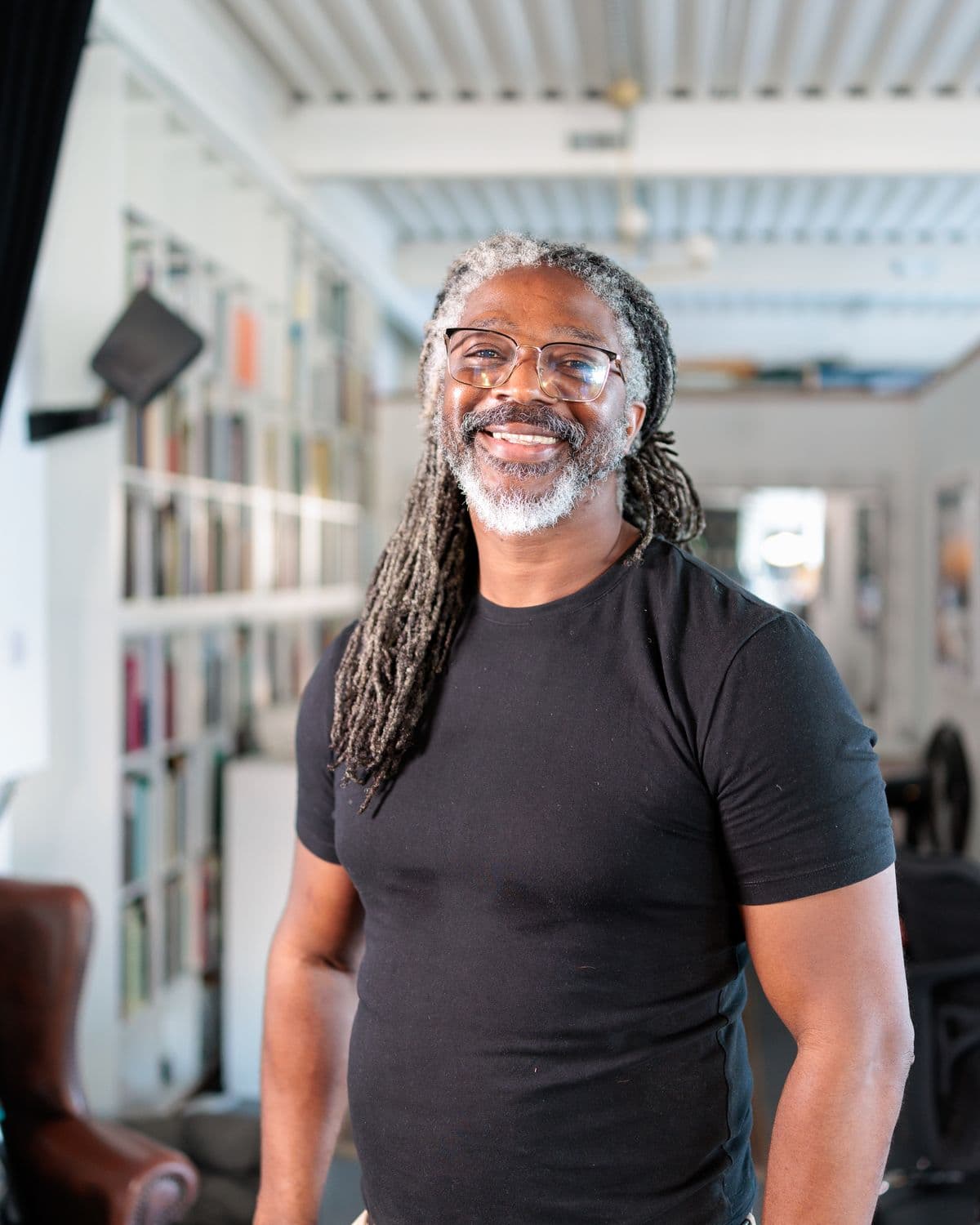 Kevan smiling at the camera in his studio, light stands and shelves of books behind him